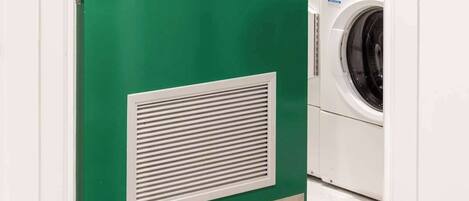 Une porte verte, à l’intérieur de laquelle se trouve un lave-linge, un panneau de commande et une grille d’aération.