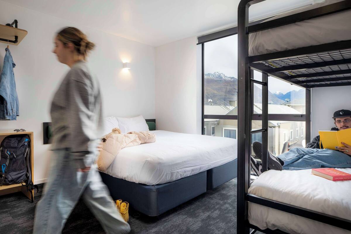 Ein modernes Hotelzimmer mit Stockbett, großem Fenster und Bergblick, Nachttisch und Kleiderschrank.