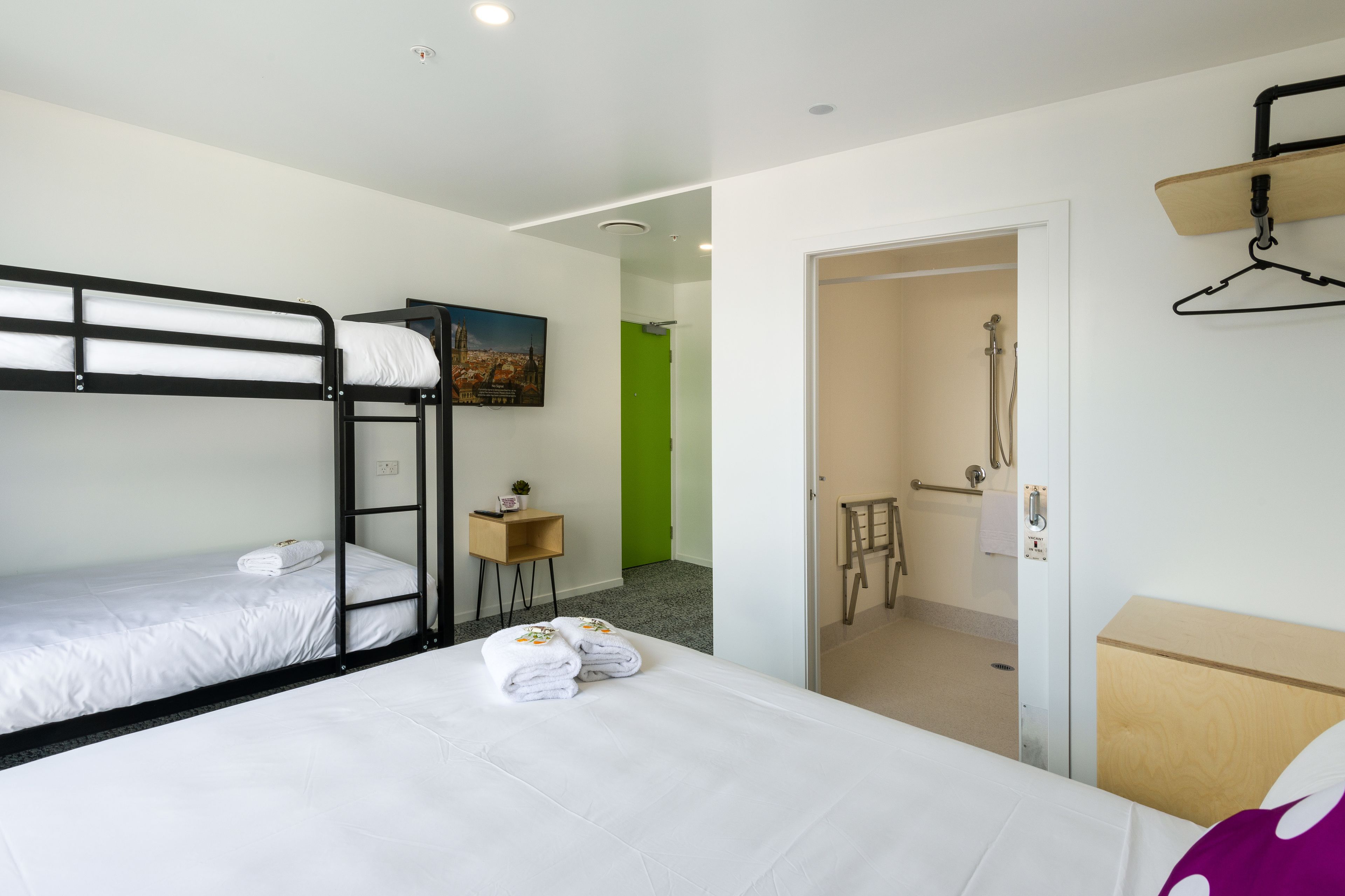 A hotel room with bunk beds, a small table with a plant, and a bathroom visible through an open door.