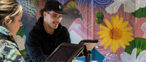 A person using a tablet at a counter with a colorful floral mural in the background.
