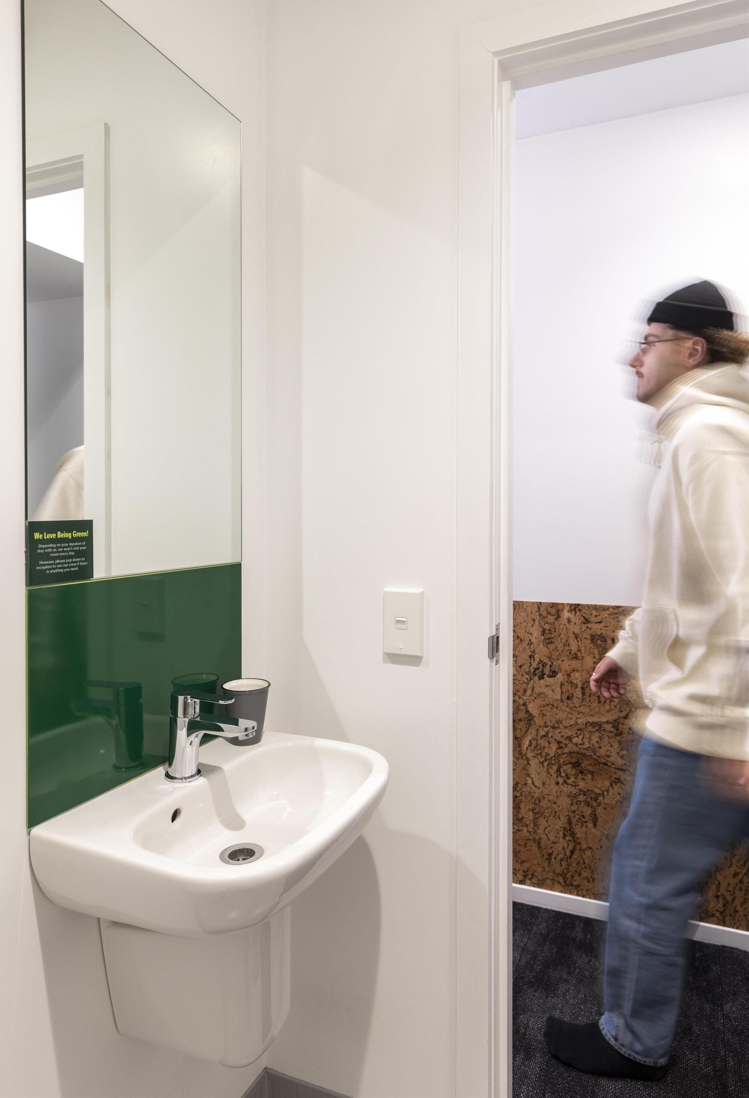 A restroom with a white sink, a mirror, and a green-tiled wall.
