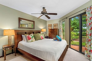 Un dormitorio con cama, ventilador de techo, mesita de noche, cómoda, ventana con cortinas y vistas al exterior.