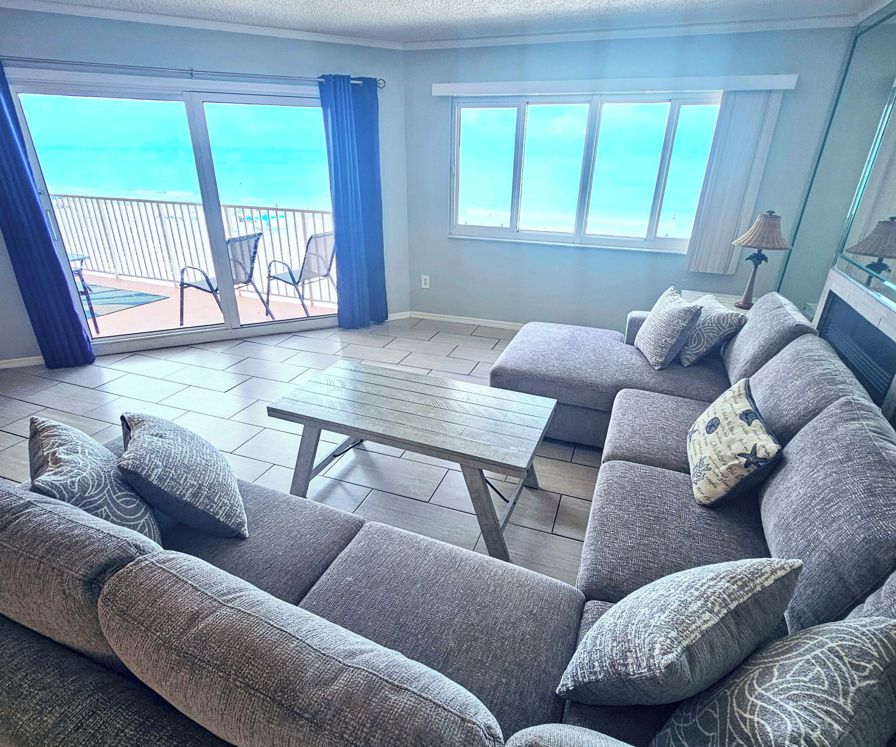 A living room with a grey sectional sofa, a coffee table, and a view of the ocean through large windows.