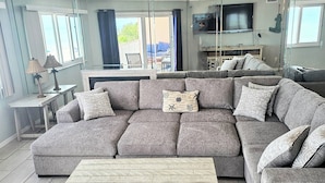 A modern living room with a grey sectional sofa, a wooden coffee table, and a TV mounted on the wall. - Beachside Gulf front 3BR,2BA condo in Indian Shores, FL Spectacular Sunsets! (Indian Shores)