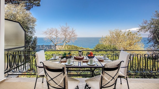 A balcony with a table set for two, overlooking a scenic view of the sea.