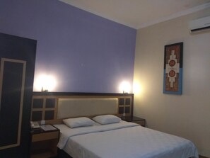A hotel room with a bed, bedside tables, a phone, and a wall-mounted air conditioner.
