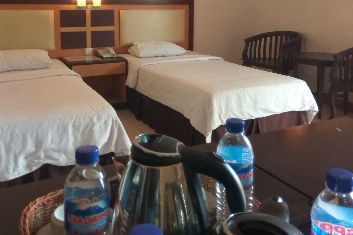 Hotellihuone, jossa on kaksi sänkyä, yöpöytä, jossa on puhelin, vedenkeitin ja vesipulloja.