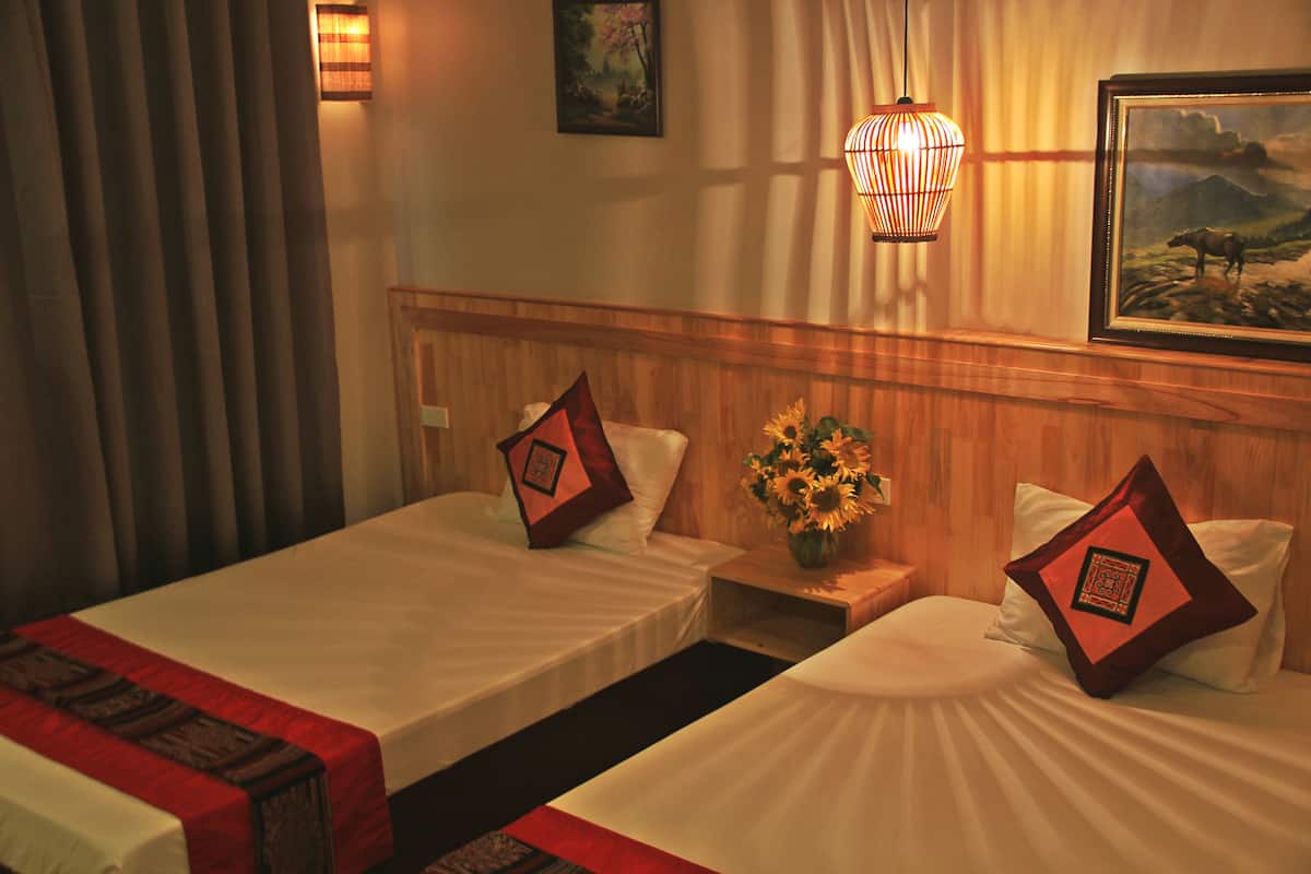 A hotel room with two beds, a nightstand with a vase of sunflowers, and a painting on the wall.
