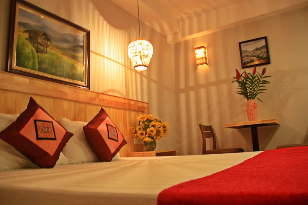 A hotel room with a bed, pillows, a vase of sunflowers, a table with a vase, and wall-mounted artwork.