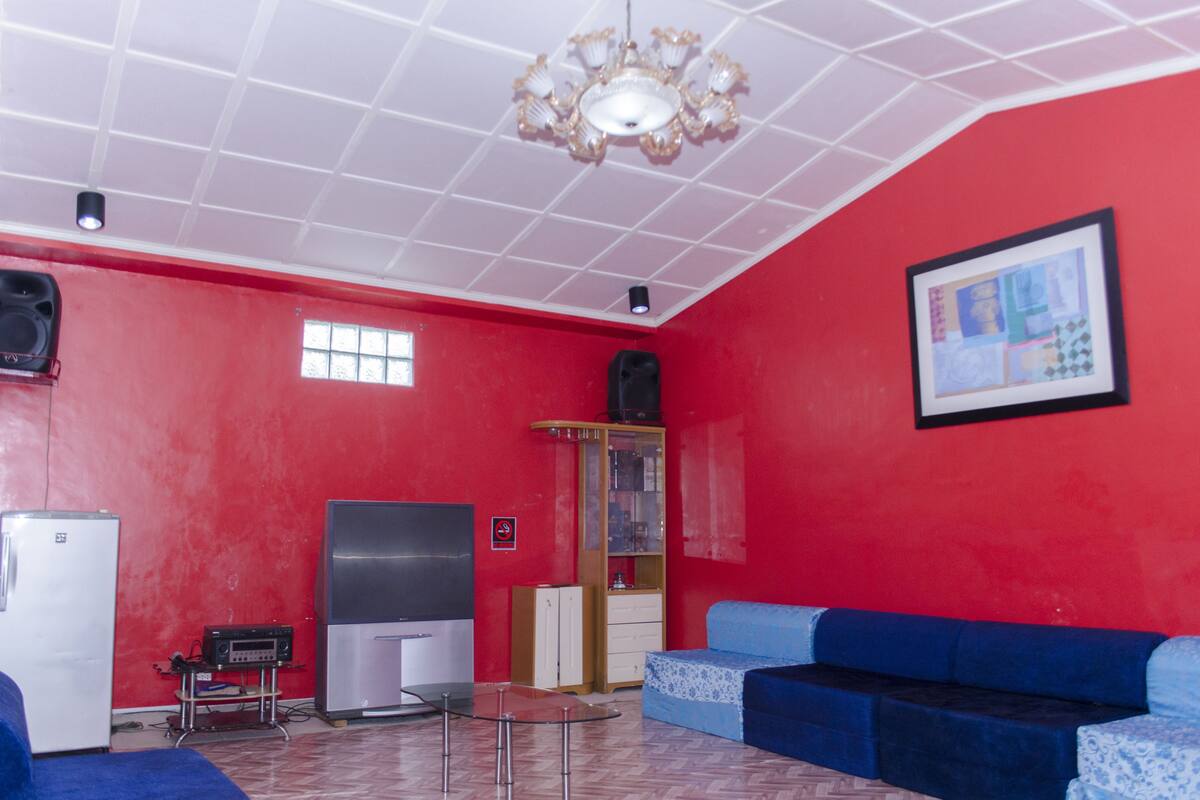 Una habitació amb parets vermelles, un sofà blau, un frigorífic blanc, una televisió i un armari.