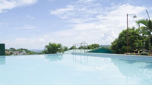 A clear swimming pool with a view of a green-roofed building and surrounding greenery. - Little Falls Inn (Tagaytay)