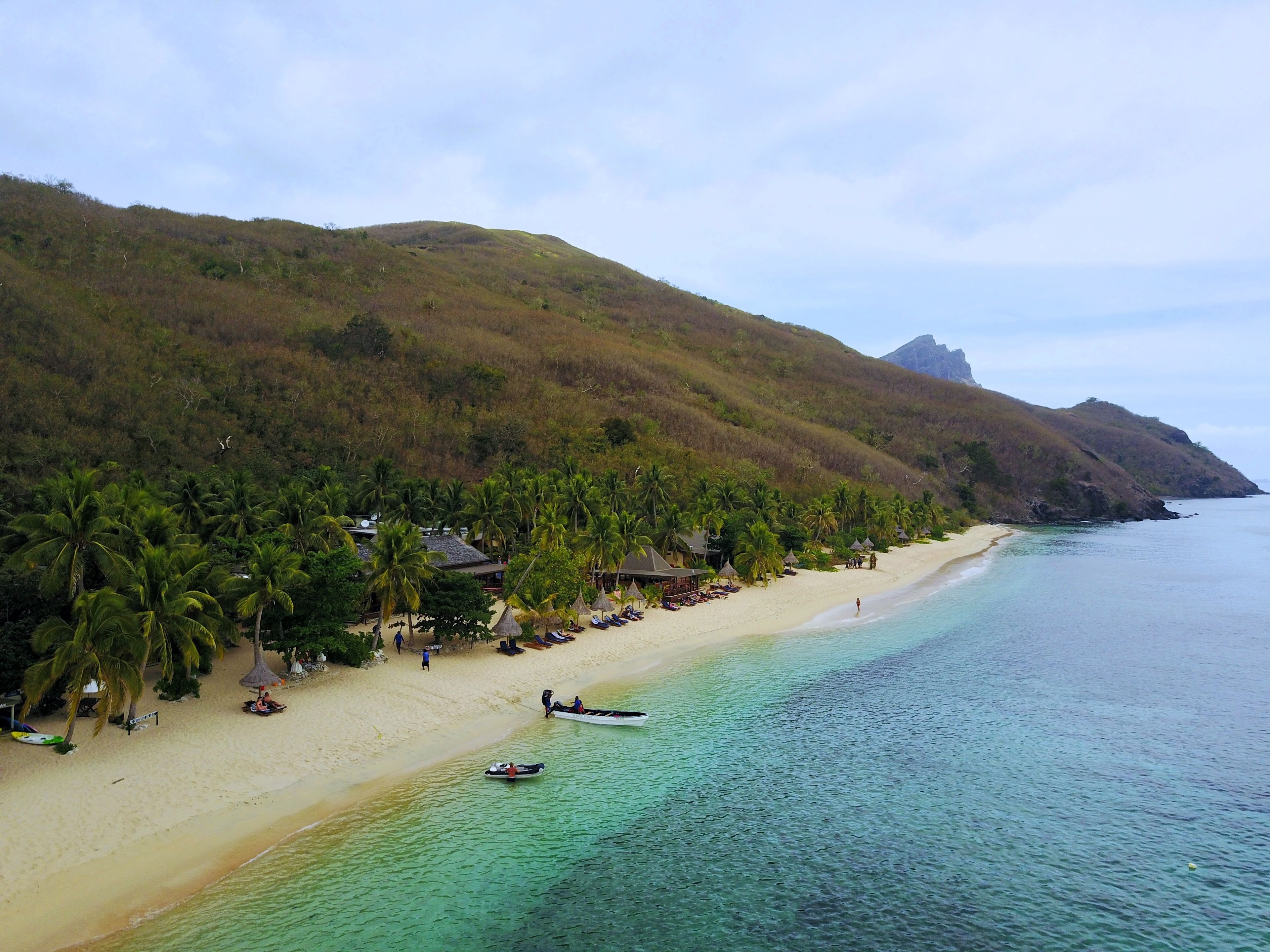 A beach with clear turquoise water, palm trees, and a few huts along the shore.