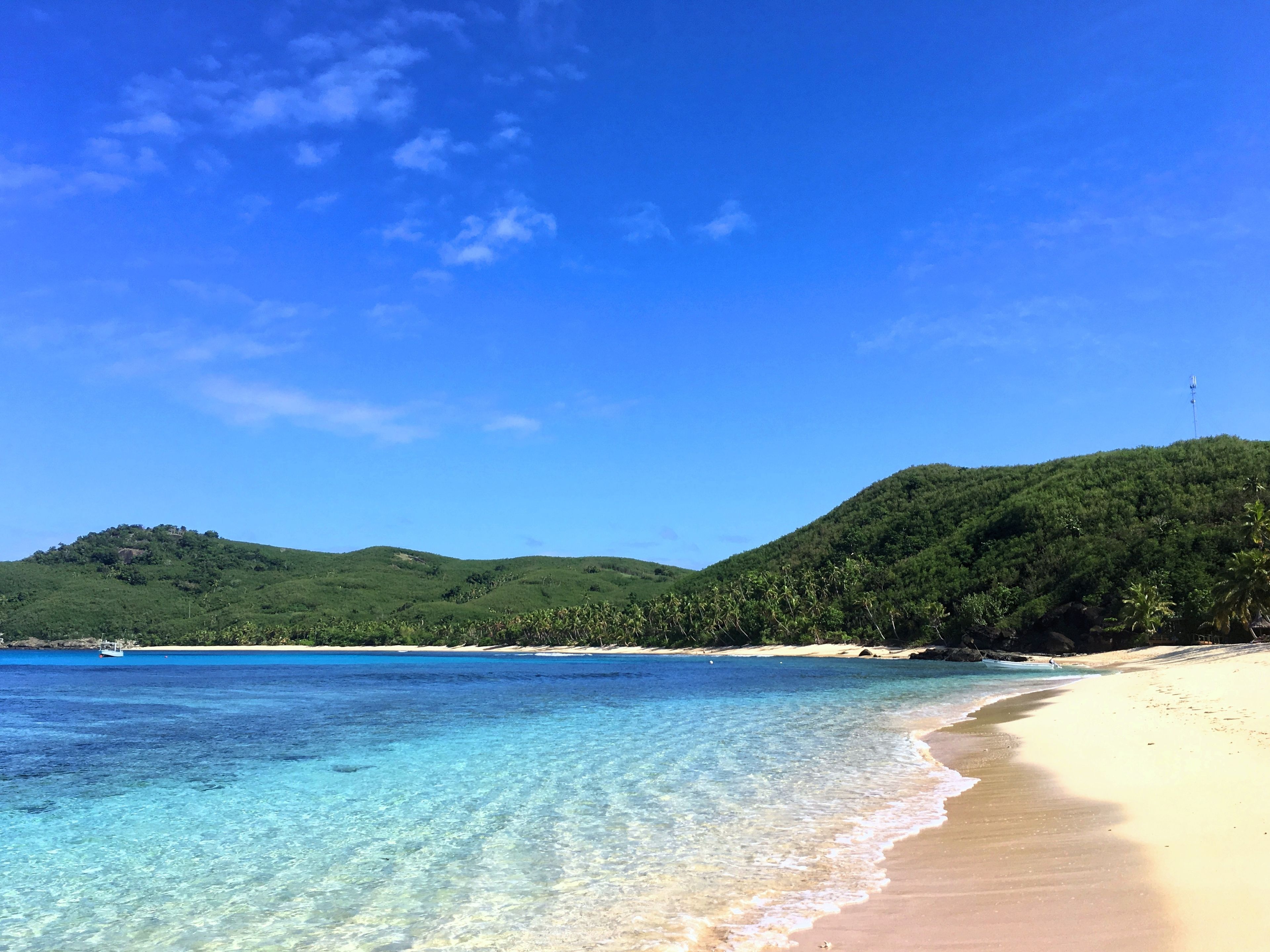 A beach with clear turquoise water, sandy shores, and lush green hills in the background.