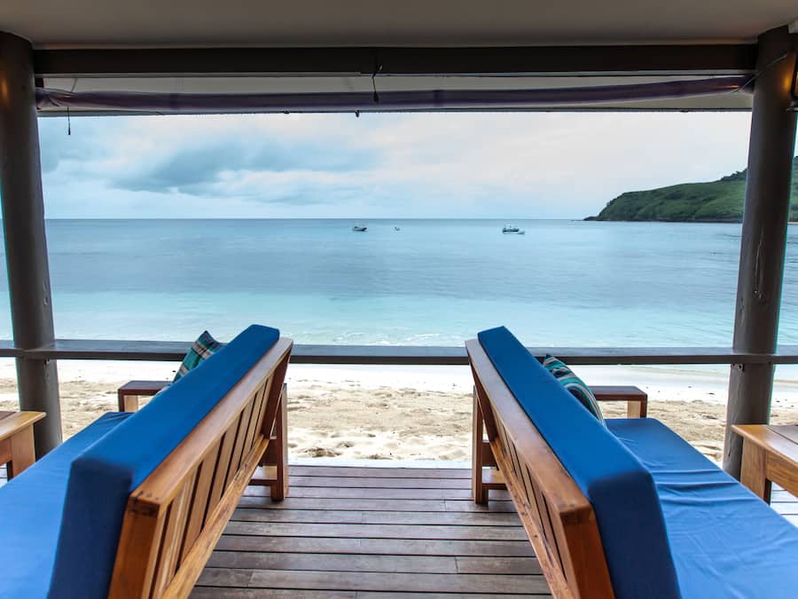 Una terraza de madera con bancos que da a una playa y al mar.