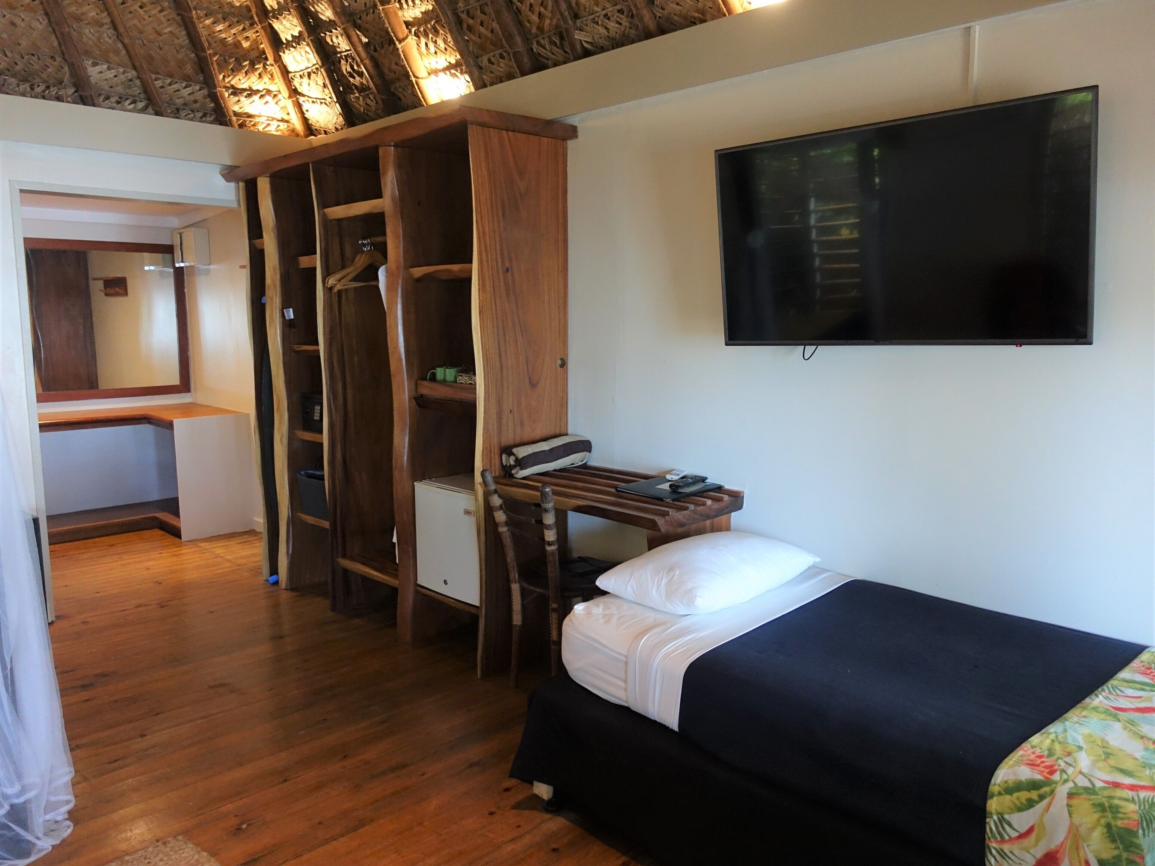 Een slaapkamer met een bed, een tv aan de muur, een houten garderobe en een bureau met stoel.