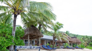 A beach resort with thatched-roof structures, lounge chairs, and a sign stating "NO LIFEGUARD ON DUTY." - Octopus Resort (Waya Island)