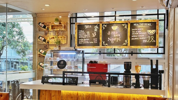 A coffee shop interior with a wooden counter, menu boards, and a coffee machine. - Best City Hotel (Yogyakarta)