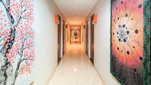 A hallway with a marble floor, flanked by two large paintings, one depicting a tree with red flowers and the other a colorful abstract design. - Best City Hotel (Yogyakarta)