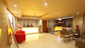 A hotel reception area with a bright desk, red seating, and a glass partition. - Best City Hotel (Yogyakarta)