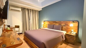 A hotel room with a wooden bed, a desk with a chair, a television, an air conditioning unit, and a nightstand with a lamp. - Best City Hotel (Yogyakarta)