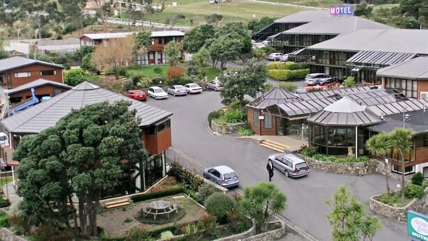Un motel con varias edificaciones, un estacionamiento y una zona ajardinada con árboles.