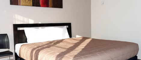 A neatly made bed with a black headboard, a black chair, and a modern abstract painting on the wall.