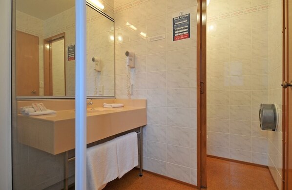 A bathroom with a sink, mirror, towel rack, and a fire action sign.