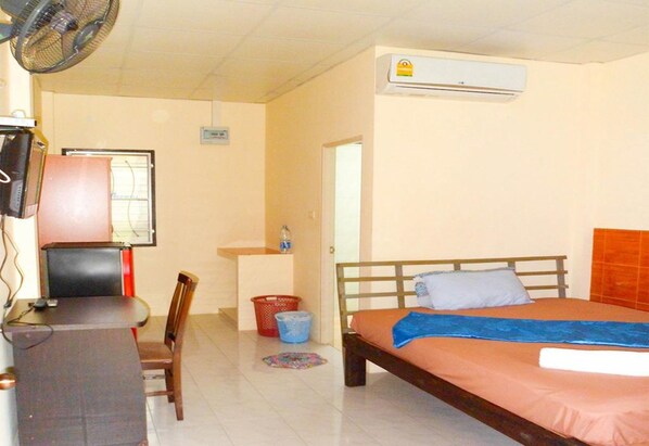 A bedroom with a bed, a desk, a chair, a fan, an air conditioner, and a window.