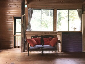 A wooden cabin room with a bed, a bench with cushions, and large windows with curtains.