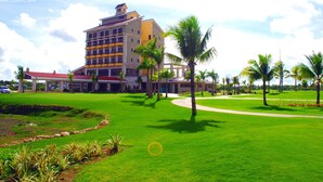 A hotel with a large building, a well-maintained lawn, and palm trees. - Queens Island Golf and Village (Medellin)