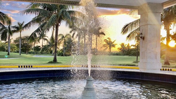 A fountain in a pool with a view of palm trees and a sunset. - Queens Island Golf and Village (Medellin)