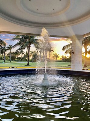 A fountain in a pool with a view of palm trees and a sunset. - Queens Island Golf and Village (Medellin)
