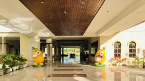 A hotel lobby with a polished floor, wooden ceiling, and two large yellow character statues. - Queens Island Golf and Village (Medellin)