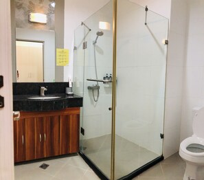 A modern bathroom with a glass-enclosed shower, a wooden vanity, and a white toilet. - Queens Island Golf and Village (Medellin)