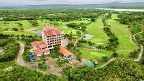 An aerial view of a golf course with a hotel featuring multiple buildings, a swimming pool, and lush greenery. - Queens Island Golf and Village (Medellin)