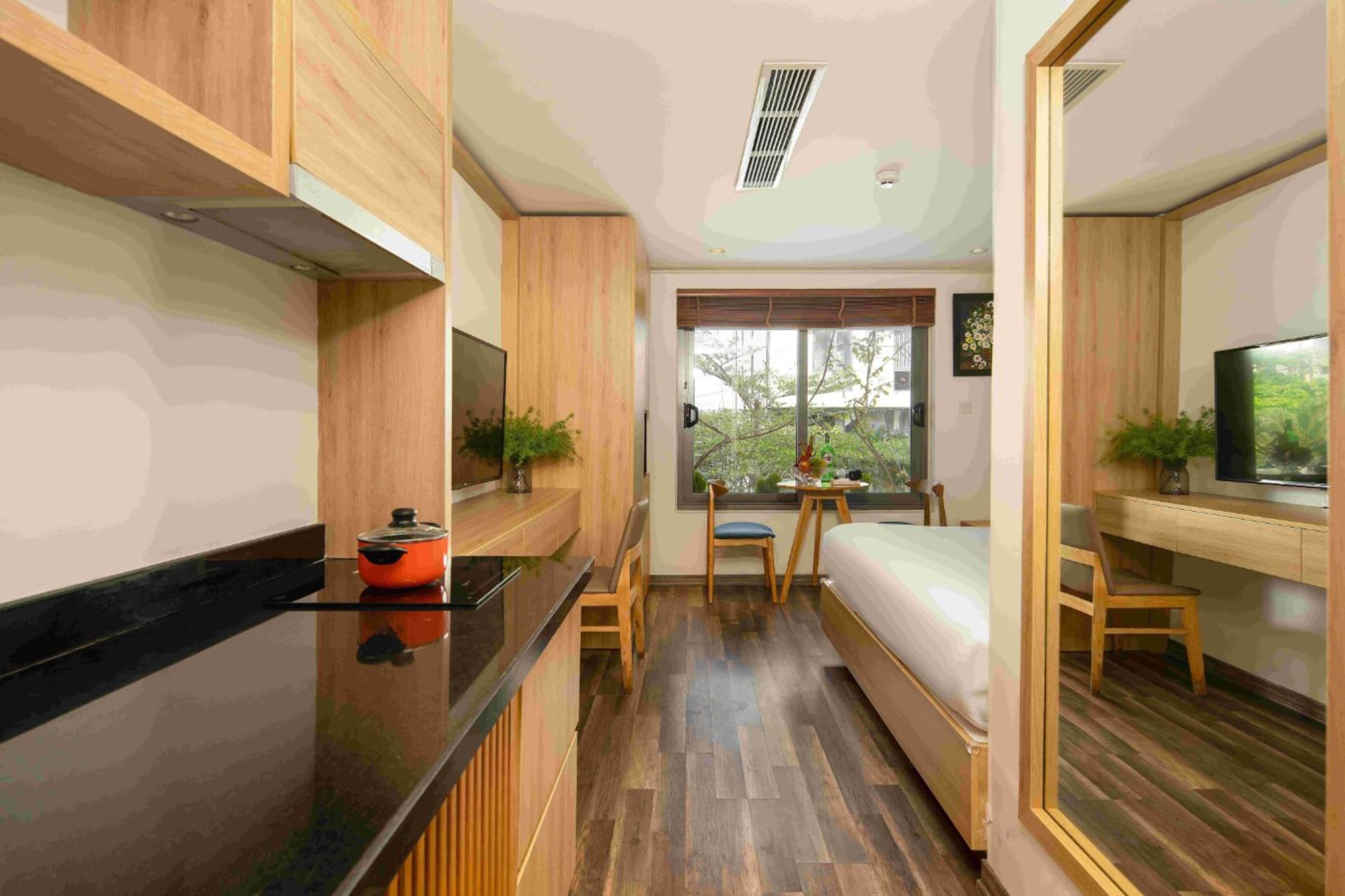 A compact room with a bed, a small table, a chair, a TV, and a window with a view of trees.