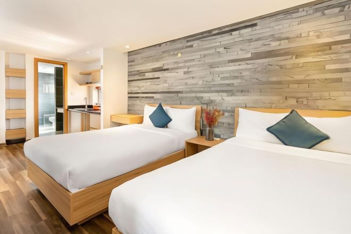Een hotelkamer met twee bedden, een houten hoofdbord, een kleine kitchenette en een houten vloer.