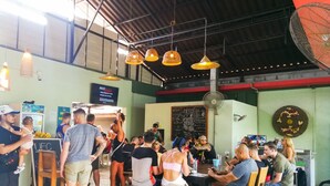A bustling indoor dining area with hanging pendant lights, a chalkboard menu, and a fan. - 2 Home Resort (Chalong)