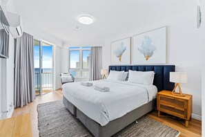 A modern hotel room with a large bed, a view of the sea, and a balcony.