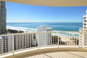 A balcony with a view of the beach and ocean, overlooking a hotel building with balconies and a clear sky.