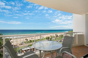 A balcony with a round table and two chairs, overlooking a beach and ocean.