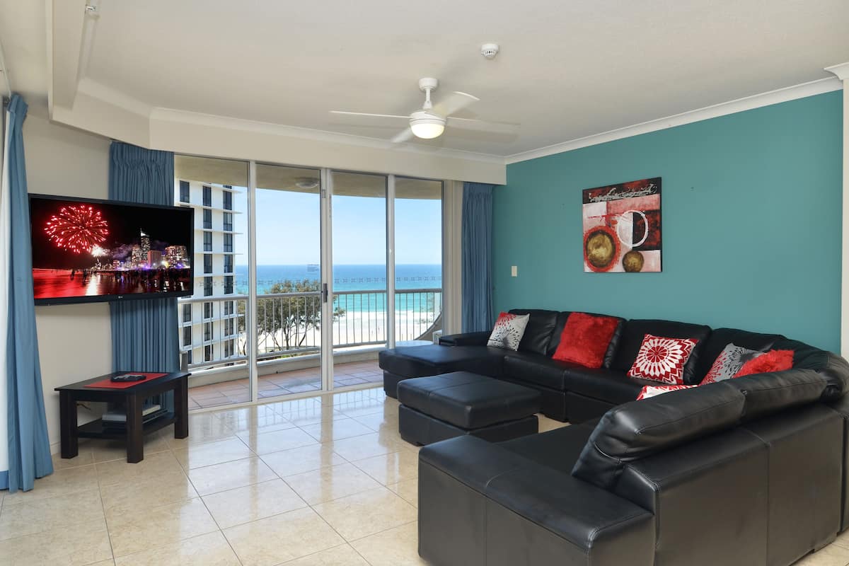 A living room with a black leather sofa, a small table, and a TV displaying fireworks.