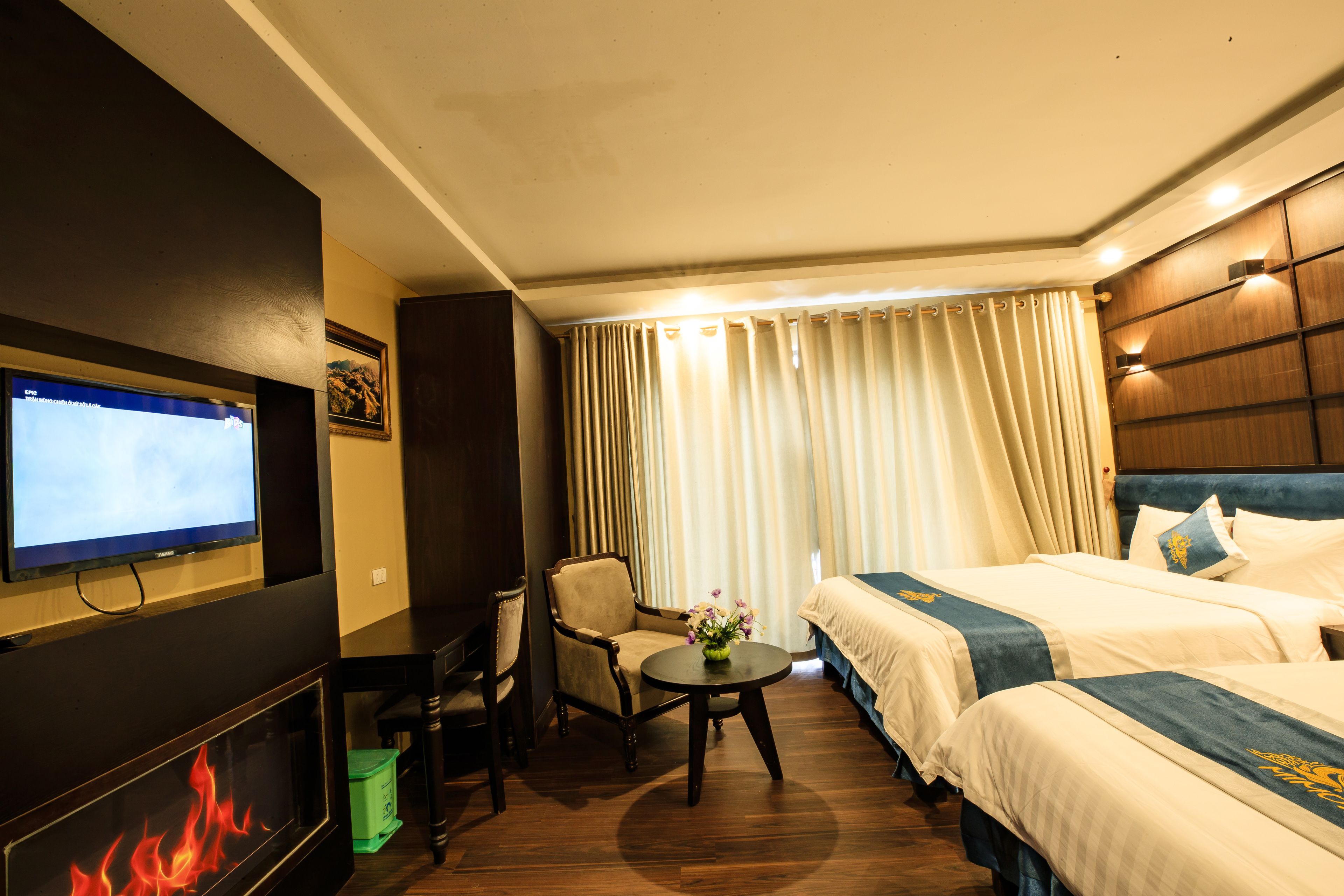 A hotel room with a TV, a fireplace, a bed, a chair, and a table with a vase of flowers.