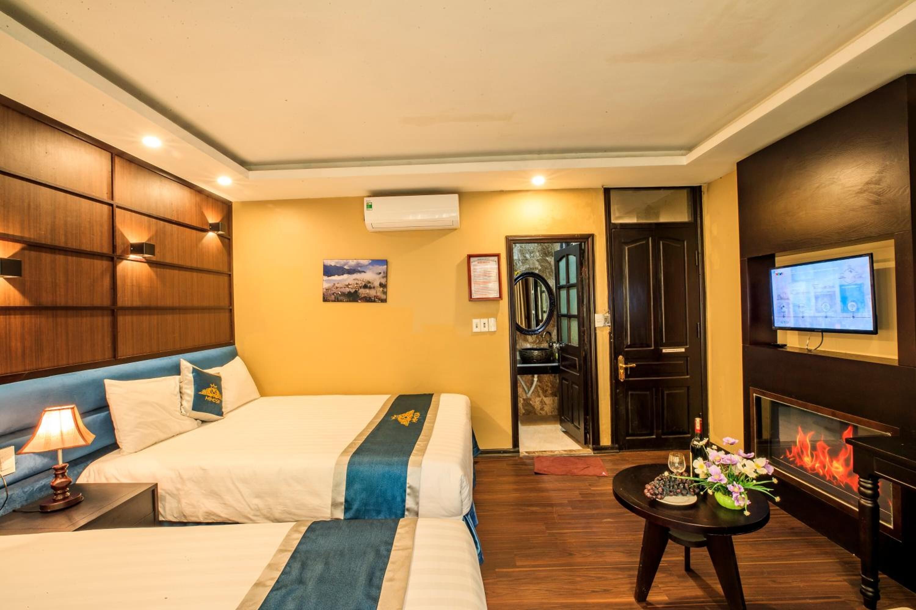 A hotel room with two beds, a TV, a fireplace, and a small table with flowers.