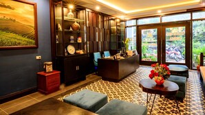 A modern interior with a reception desk, seating area, and large windows offering a view of greenery. - Sapa Mimosa Hotel (Sa Pa)