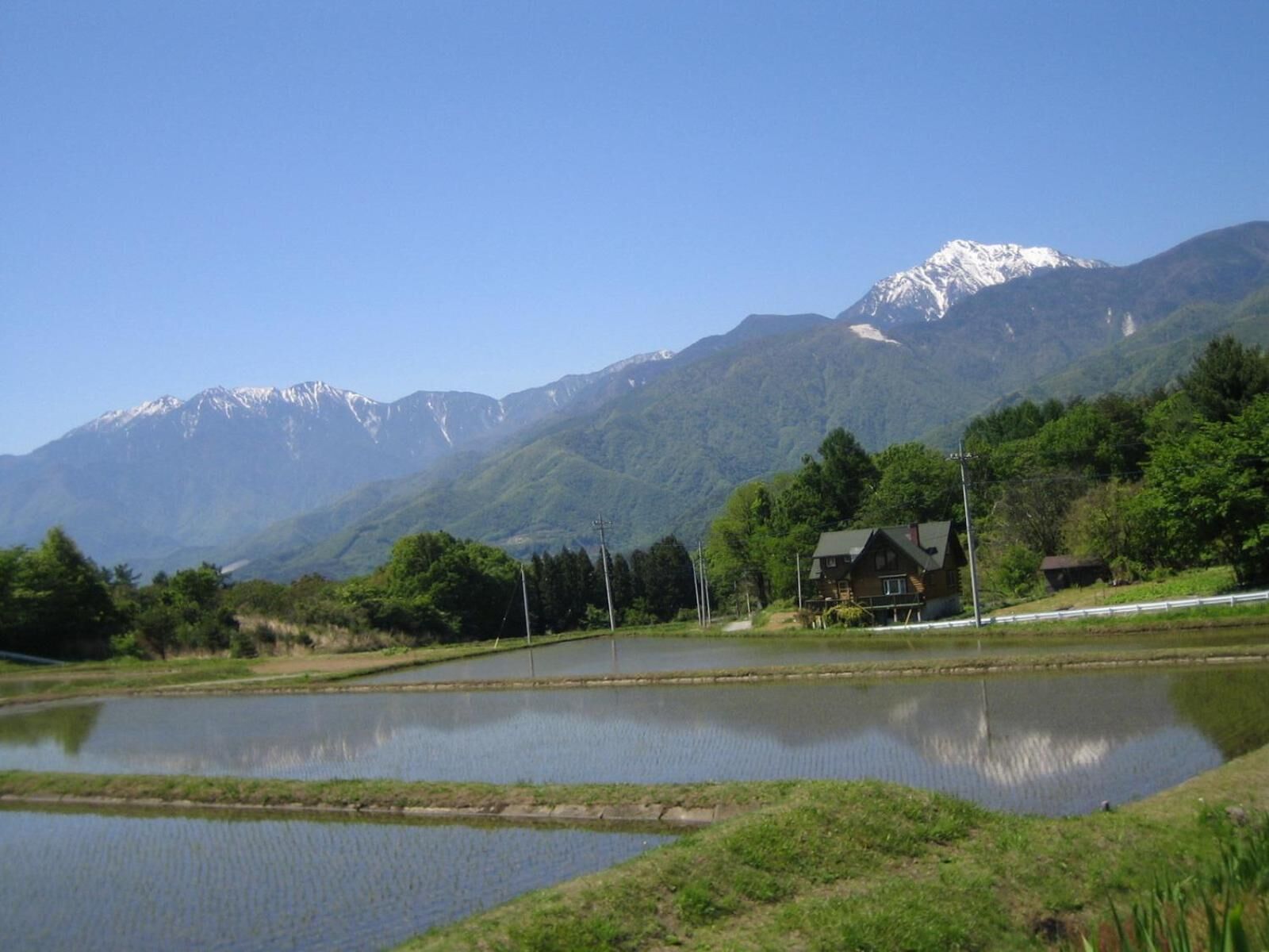A house with a pond in front, surrounded by mountains and greenery.