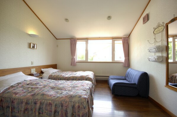 A room with two beds, a sofa, a window with curtains, a mirror, and a wall-mounted towel rack.