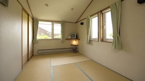 A room with tatami mat flooring, a heater, a television, and a window with curtains. - Pension Field (Hokuto)