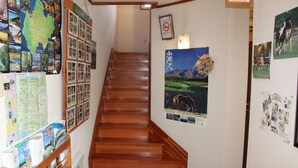 A wooden staircase in a hallway with a map and various posters on the walls. - Pension Field (Hokuto)