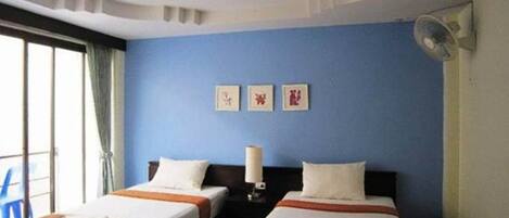 Habitación de hotel con dos camas, ventilador de techo y ventana con cortinas.